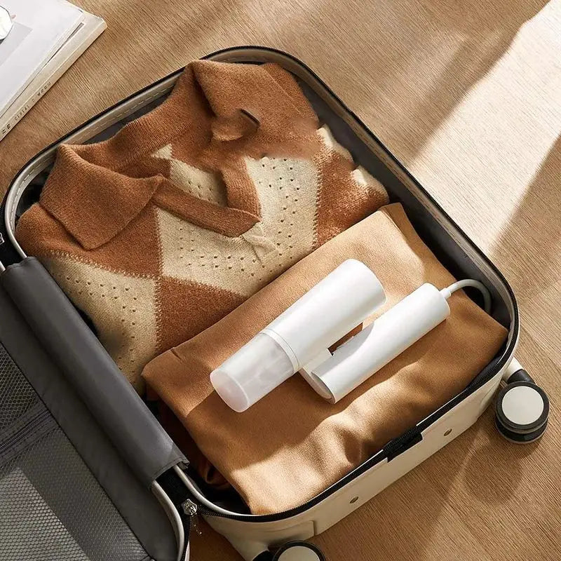 Open suitcase with folded clothes and a hair straightener on a wooden floor